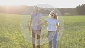 A guy and a girl are walking on the grass, holding hands