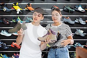 Guy with girlfriend, view specialized shoes in store, near showcase with summer trecking cross-shoes