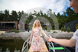 The guy gives his hand to the girl, helps to get into the boat on the pier