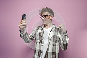 guy with glasses holds smartphone and shows celebrating the victory, winner with the phone shows success