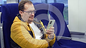 guy in glasses looks social media, texting messages using cell phone while riding home by train