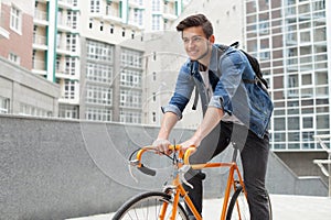 The guy goes to town on a bicycle in blue jeans jacket . young man an orange fix bike