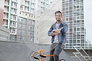 The guy goes to town on a bicycle in blue jeans jacket . young man an orange fix bike