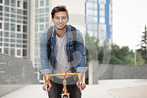 The guy goes to town on a bicycle in blue jeans jacket . young man an orange fix bike