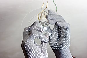 A guy in gray gloves is spinning a light bulb. Replacing the light bulb.