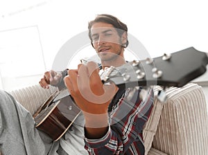 Guy with guitar sitting on sofa in living room. concept of a lifestyle