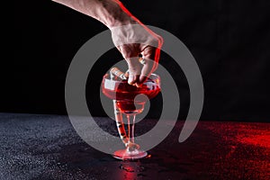 Guy hand keeps a little snake near a glass with red liquid in the dark room