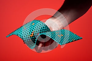 The guy hands holds a green massage mat with metal needles and rubber, compresses, on a red background. For relaxation, health.