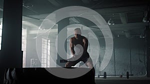 Guy having fitness training with hammer. Man hitting tire with sledgehammer