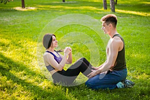 guy helps the girl to do the press exercise, sitting on the lawn in the park