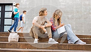 Guy helps girl to solve the school problem while sitting on stone stairs in front of school
