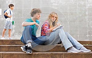 Guy helps girl to solve the school problem while sitting on stone stairs in front of school