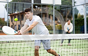 Guy hitting two handed backhand during paddle tennis match