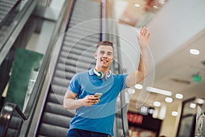 Guy holding mobile phone and smiling while walking down the mall