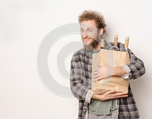 Guy is holding a paper bag with bottles of wine. Smiling he looks into camera. Concept of a good time, a friendly
