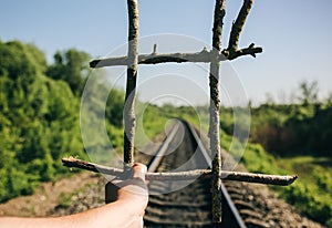 Guy is holding prisons grate made from wooden sticks. Freedom concept photo with rail tracks in the green field. Railway transport