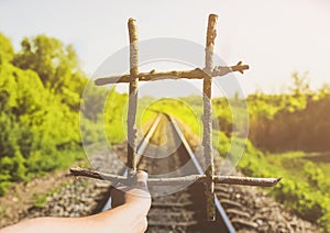 Guy is holding prisons grate made from wooden sticks. Freedom concept photo with rail tracks in the green field. Railway transport