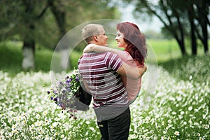 The guy holds the girl in his arms in a green park with white daisies