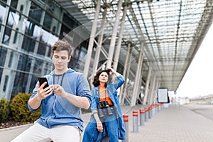 The guy holds the phone in his hands. Young cute couple - a boy and a girl travel around the city with binoculars in