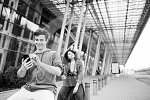 The guy holds the phone in his hands. Young cute couple - a boy and a girl travel around the city with binoculars in their hands.