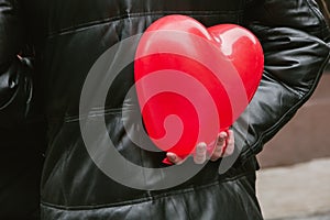 The guy holds a red heart ball in his hand behind his back