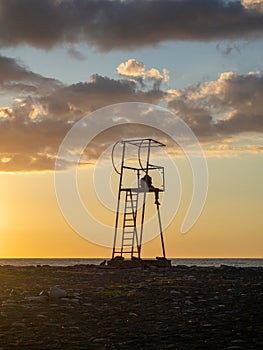 guy in a hood on a rescue tower. Silhouette of a young lonely man. Silhouette of a person looking out to sea at sunset.