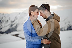 Guy hugs a girl against a background of gray snow-capped mountains