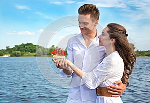 Guy hugs a girl near the water and holding her hand. Girl holding a boat with red sails.