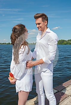 Guy hugs a girl on a wooden pier near the water.