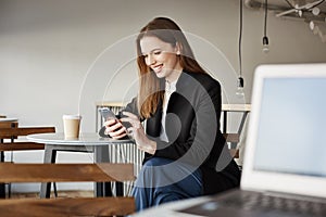 Guy with laptop gazing at attractive woman sitting next to him in cafe. Side-shot of beautiful stylish girl messaging