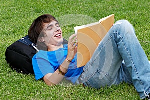 Guy laying on the grass and reading a book