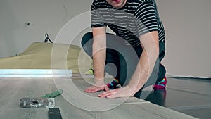 Guy laying laminate boards on floor with hammer.