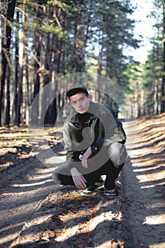 A guy in a leather jacket and cap on a road in a pine forest