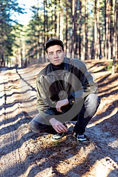 A guy in a leather jacket and cap on a road in a pine forest