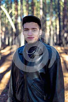 A guy in a leather jacket and cap on a road in a pine forest