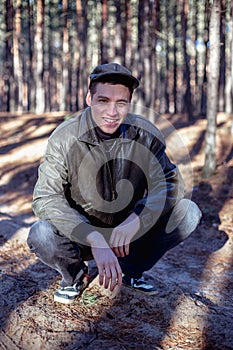 A guy in a leather jacket and cap sits on a road in a forest