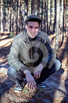 A guy in a leather jacket and cap sits on a road in a forest