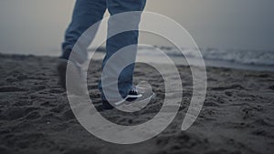 Guy legs in fashionable sneakers walking on beach. Man feet exploring sea coast