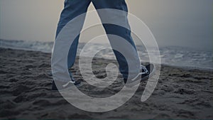 Guy legs in fashionable sneakers walking on beach. Man feet exploring sea coast