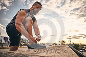 The guy lifted and bent his knee to tie the lace on the sneaker while jogging against the backdrop of the city and sunrise. Sport