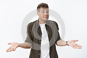 Guy lifting hands in dismay sideways and shrugging unbothered giving friendly unaware smile at camera as being uncertain