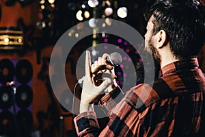 Guy likes to sing in dark karaoke hall. Musician with beard singing song in karaoke, rear view. Rock singer concept. Man