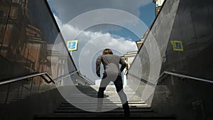 Guy with long hair go up the stairs from the underground passage. Joyful bearded man walks dancing up the stairs out of