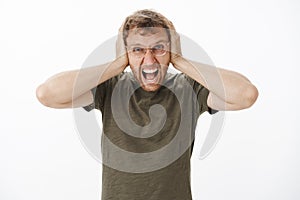 Guy lose temper being with loud noises at night yelling out loud with angry outrage expression covering ears with