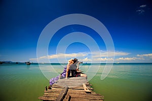 Guy Make Photos with Blond Girl That Leans on Wooden Pier