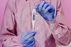 A guy in a mask and a medical glove holds a thermometer. Pink background.
