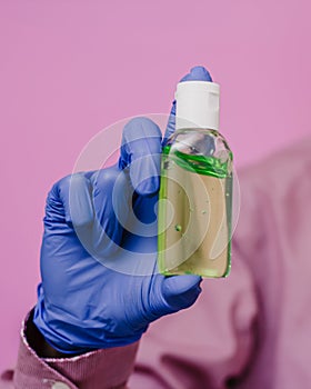 A guy in a medical glove holds a bottle of antiseptic sanitizer. Pink background. Antibacterial effect, disinfection.