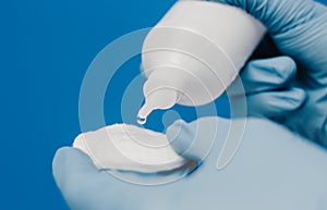 A guy in a medical glove holds cotton pads and a second-hand bottle. Blue background. Medical and cosmetology content