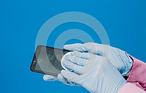 A guy in a medical glove wipes his phone with cotton pads. Blue background. Antibacterial effect, disinfects, disinfects