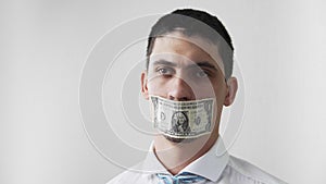 The guy with the mouth sealed with dollar bill turns and looks into the camera. The theme of bribery and corruption. Fraud.